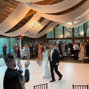 A bride and groom enter their reception to applause beneath a chandelier and draped ceiling