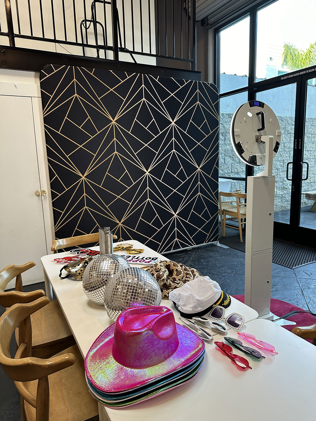 Photo booth set up in front of a black and gold geometric backdrop with a table of props